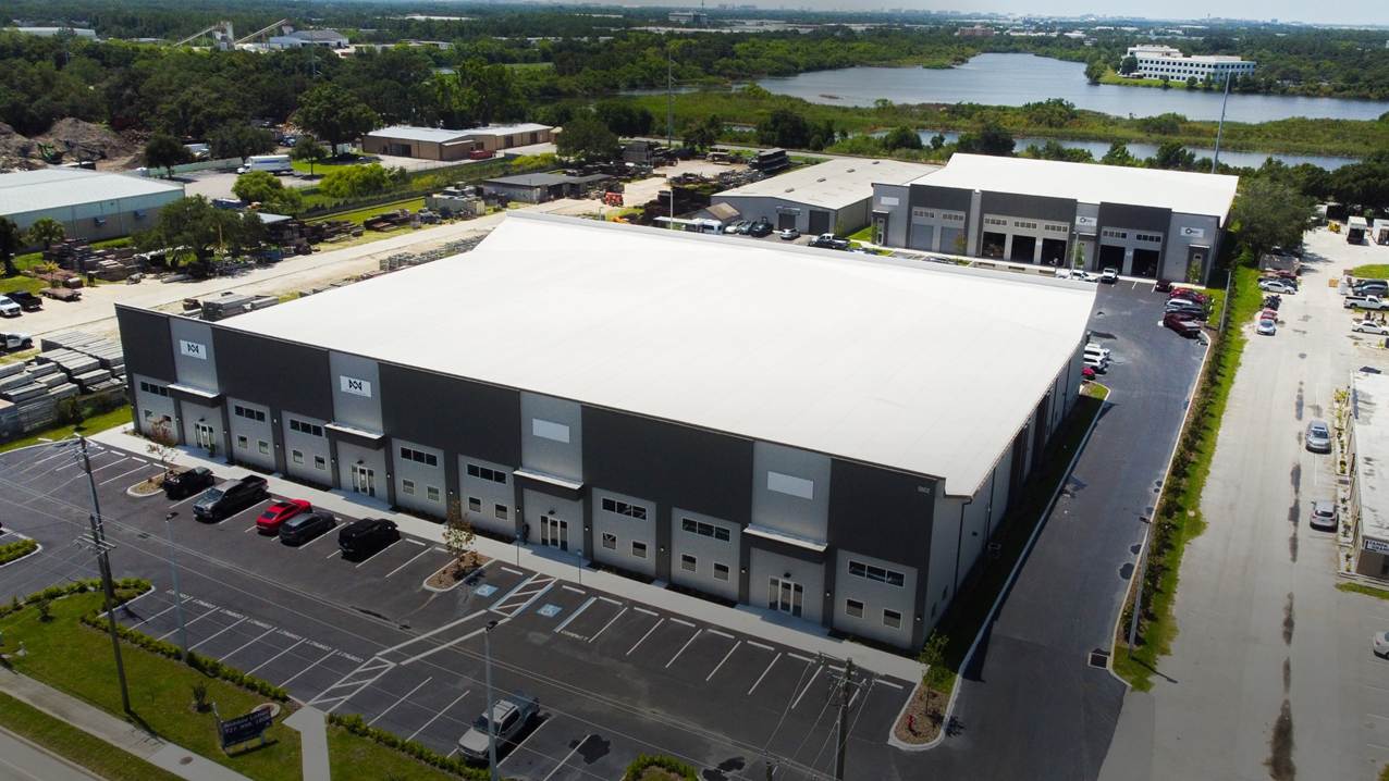 Aerial view of industrial buildings with loading bays, parking, and a lake beyond
